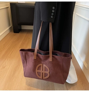 Detail of dark red-brown suede tote bag featuring a large circular geometric logo