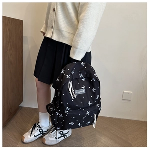 Sac à dos d'école noir avec motifs de nœuds blancs présenté de profil en situation