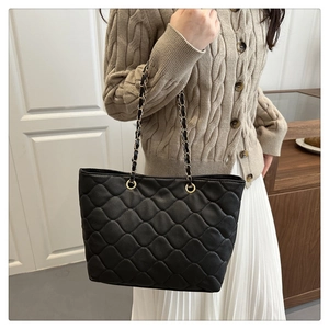 Detail of black quilted tote bag with gold chain strap shown on a model for daily commute