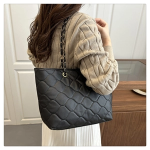 Detail of a black quilted tote bag with gold chain strap worn by a model in a cozy room