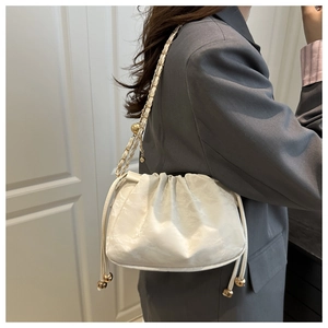 Détail d'un sac seau blanc plissé avec cordon doré sur une veste de blazer grise