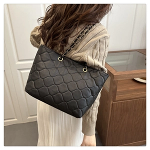 Detail of black quilted tote bag with golden chain strap and classic diamond pattern