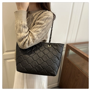 Close-up of black quilted tote bag with wave pattern stitching and chain shoulder strap