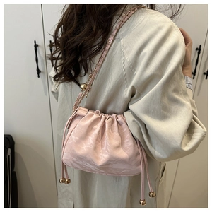Pink drawstring dumpling bag featuring pleated texture and gold chain strap with ball detail