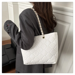 Side view of white quilted tote bag with chain strap on model for size reference