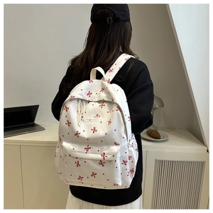Détail du sac à dos blanc à motifs de nœuds rouges avec poche avant et étiquette mode