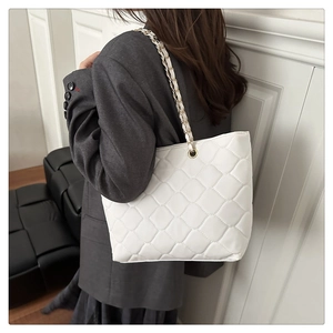 Detail of white quilted crossbody bag with gold chain strap worn by a model