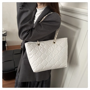 Detail of white quilted tote bag with chain strap shown on model in a minimalist setting