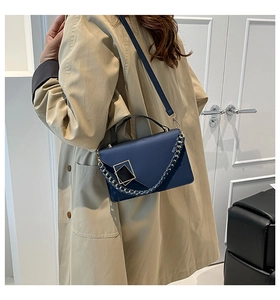 Detail of dark blue leather crossbody bag with gold buckle and woven chain handle