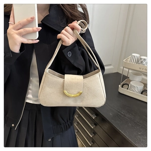 Detail of minimalist beige suede baguette bag with gold crescent metal clasp and slim strap
