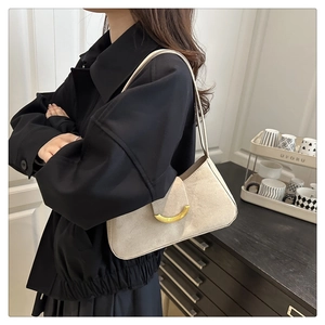 Close-up of minimalist beige suede baguette bag with a half-moon golden metal buckle