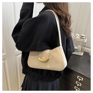 Close-up of beige suede shoulder bag with golden crescent buckle on model in home setting