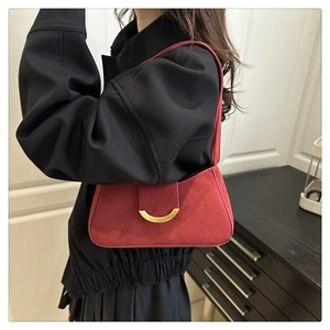 Detail of red suede shoulder bag with golden half-moon buckle worn by a model