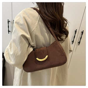 Détail du sac baguette en daim marron foncé avec boucle dorée porté à l'épaule par le mannequin