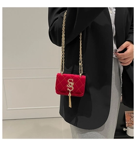 Détail du sac bandoulière en velours rouge avec boucle dorée en S et pendentif pompon