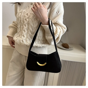 Close-up of black suede baguette bag featuring a golden half-moon metal buckle detail
