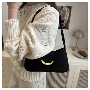 Close-up of minimalist black baguette bag with gold crescent buckle on shoulder
