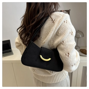 Detail of black suede shoulder bag with gold metal buckle on a white knit sweater