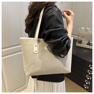 Detail of a large canvas tote bag with white leather straps shown on a model's shoulder