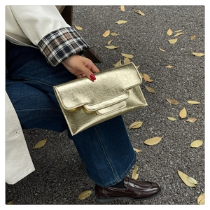 Nahaufnahme der goldenen rechteckigen Clutch mit Faltentextur in herbstlicher Umgebung