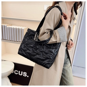 Detalle de un gran bolso tote acolchado negro combinado con una gabardina beige