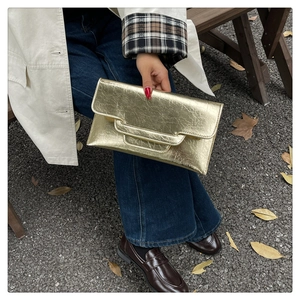 Modische goldene Clutch in Umschlagform mit Faltenstruktur im Freien von einem Modell gehalten