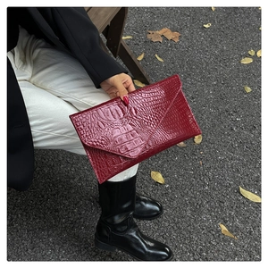 Close-up of red crocodile pattern envelope clutch bag held by model on outdoor bench