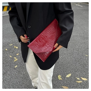 Detail einer tiefroten Briefumschlag-Clutch mit Krokoprägung und Klappverschluss