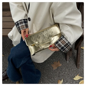 Nahaufnahme der goldenen Clutch mit Knister-Textur, von einem Model draußen gehalten