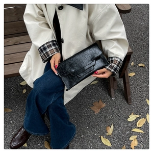 Detail einer schwarzen gefalteten Leder-Clutch, die ein Model im Herbstpark hält