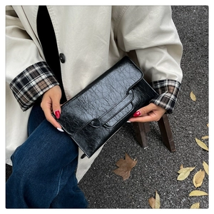 Detail einer schwarzen glänzenden Clutch aus Kunstleder mit eleganter Faltenstruktur