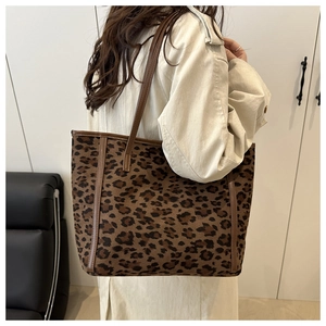 Large leopard print tote bag with brown leather straps shown on a model's shoulder