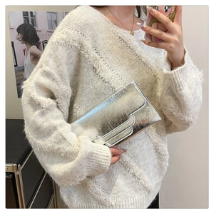 Nahaufnahme einer silbernen Clutch mit Plissee-Textur, getragen von einem Model im Strick