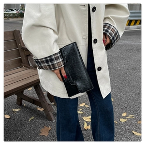 Schicke schwarze Umschlag-Clutch aus PU-Leder mit Faltenoptik von einem Model getragen