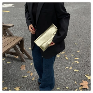 Detail einer goldenen Clutch im Umschlag-Design mit Plissee-Struktur in der Hand