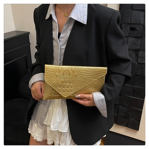 Golden envelope clutch bag with crocodile print texture held by a model in formal attire
