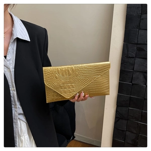 Dettaglio della trama a coccodrillo dorata su una pochette a busta tenuta a mano dalla modella