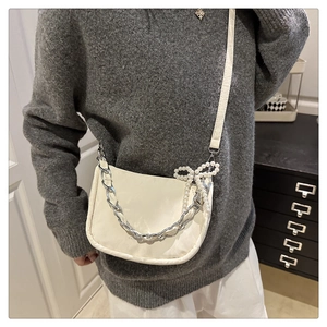 Détail du sac bandoulière crème avec poignée chaîne argentée et breloque nœud perlé
