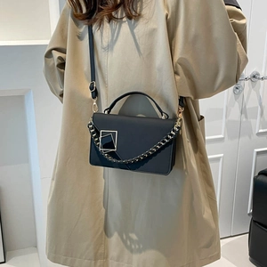 Fashionable black matte crossbody bag with woven chain strap on a trench coat model