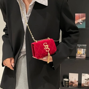 Sac bandoulière en velours rouge matelassé avec logo S doré porté sur un blazer noir