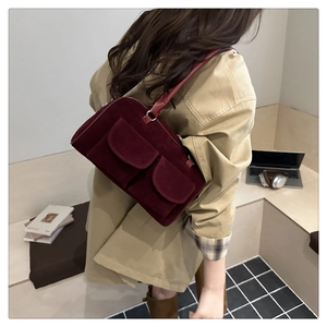 Close-up of burgundy suede shoulder bag with dual front pockets on a model