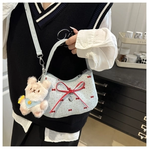 Detail of light blue crossbody bag with red bows, silver heart charm, and plush bear