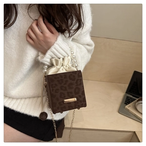 Detail of leopard print crossbody bag with pearl handle and drawstring on wooden stairs