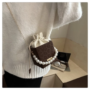 Close-up of leopard print bucket bag with pearl handle and golden chain on a beige sweater
