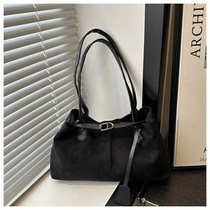 Detail of black faux suede tote bag featuring silver buckle strap and long tassel decor