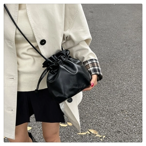 Dettaglio di una borsa a secchiello nera con coulisse, pieghe in pelle e tracolla sottile