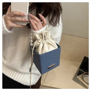 Detailed view of blue box bag with pearl handle and cream drawstring pouch insert