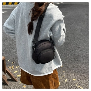 Outdoor view of a black nylon crossbody bag featuring double-zipper structure and round pocket