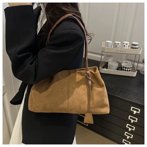 Close-up of caramel brown suede underarm bag with slim shoulder strap and tag
