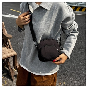 Outdoor street view of a compact black nylon crossbody bag with adjustable shoulder strap